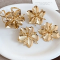 Primo piano di anelli e orecchini a forma di fiore in oro metallico su piatto bianco. - Anello Orecchini e Bracciale / Set da 4 pezzi / Oro