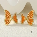 Macro shot of gold butterfly earrings with orange enamel wings and sparkling zircons - Orange