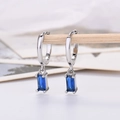 Detail of silver hoop earrings featuring rectangular deep blue zircon drops on a wood stand - Platinum Plated Blue Zirconia