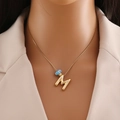 Vue détaillée d'un collier en or 18 carats avec initiale M et perle d'œil bleu sur modèle - Lettre M Or