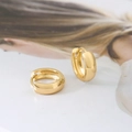 Close-up of polished gold U-shape huggie earrings on a stylish magazine background - Gold