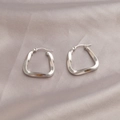 Polished silver-tone twisted geometric oval earrings on soft grey satin background - Geometric Twisted Style / Silver
