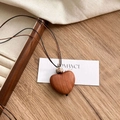 Collier artisanal en bois de santal avec pendentif cœur sur fond en bois rustique - Collier Coeur en Palissandre