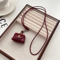 Mini donkerrode leren hanger ketting met gouden drukknop en een geweven koord - Rode Mini Tas Ketting