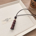 Bamboo-shaped sandalwood pendant necklace with a black braided cord on a tray - Red Sandalwood Hollow Bamboo Joint Necklace (Openable)