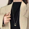 Elegante gouden ronde hanger lange ketting op model met zwarte coltrui en blazer jas - Gouden Tas Hanger Ketting