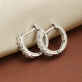 Close-up of silver-tone zircon pavé hoop earrings on textured beige and brown fabric - Silver