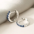 Macro shot of silver hoop earrings featuring a row of inlaid deep blue cubic zirconia - Blue