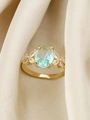 Macro di anello dorato con zircone blu ovale e dettagli floreali su seta elegante - US 6 / Oro