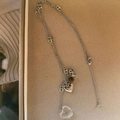 Détail d'un long collier argenté avec pendentif coeur et perles de pierre sur fond neutre - Style Cœur Blanc