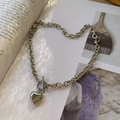 Collar de corazón de acero inoxidable plateado con cierre de barra sobre un libro - Collar de Corazón con Broche de Palanca