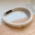Detailaufnahme eines beigen Stoffstirnbands mit goldener Rose und Logo auf Holzuntergrund - Verdickter Stil Mit Akzenten / Beige