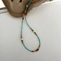 Macro detail of beaded necklace showing blue stones, pearls, and gold logo tag - Titanium Steel Turquoise Natural Stone Chain