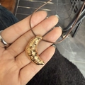 Golden croissant pendant on dark brown braided cord necklace held in hand - Gold Croissant Necklace