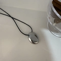 Minimalist silver oval pendant necklace with a black cord on a white desk - Oval Faceted Style