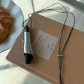 Detail der minimalistischen Halskette mit schwarzer Kordel auf einem Notizbuch - Schwarzes Holz Metall Rolle Stil