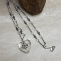 Macro detail of transparent heart pendant with crystal cross on vintage silver chain - Clear