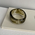 Irregular resin bangle with green marble pattern on a white fabric book background - Wide Wave Style / Ink Flower Green