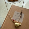 Detail of golden whale pendant with red bead on a thin woven cord necklace - Matte Gold Fish with Beige Cord