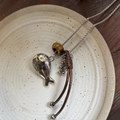 Detail der Fisch-Halskette mit Tigerauge-Stein auf Keramikteller vor Holz Hintergrund - Kleiner Fisch Quaste Halskette