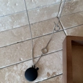 Detail of silver chain necklace with black matte circular pendant and T-bar clasp closure - OT Buckle / Black
