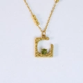 Detalle macro de collar de oro de 14k con gema verde en colgante de letra C martillado - Forma de letra cuadrada con circonita verde / Verde Fruta