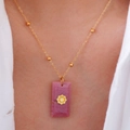 Dettaglio di una collana vintage dorata con ciondolo quadrato in pietra rosa sul collo - Rodocrosite