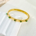 Detailed shot of 18K gold sunflower bangle with green gemstones on white stone - Green Gemstone Style (B939)