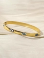 Detailed shot of gold evil eye bangle with blue enamel on silk fabric background - Evil Eye Style