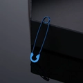 Detailed close-up of blue safety pin earring with metallic finish on dark reflective surface - Blue