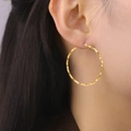 Boucles d'oreilles créoles dorées torsadées en spirale portées par un mannequin de mode - 54mm / Acier