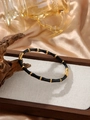 Detail view of black and gold bamboo-style stainless steel bracelet on a wooden tray - Black