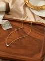 Macro view of gold paperclip chain necklace with a rectangular clear crystal pendant - White
