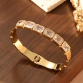 Detail of 18K gold-plated bangle with six rectangular zircons on dark wood background - 18K Gold / White