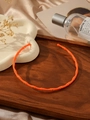 Detailed shot of orange bamboo-joint steel choker with gold accents on wooden tray - Orange
