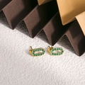 Dettaglio di orecchini ovali in titanio dorato con zirconi verdi e centro cavo - Zirconia Verde (ZHE1981)
