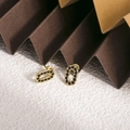 Détail de boucles d'oreilles ovales dorées avec pavage noir sur fond de texture géométrique - Zirconia Noir (ZHE1981)