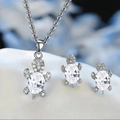 Detailed close-up of sea turtle necklace and earrings set with white stones and silver finish - White