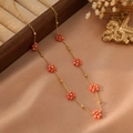 Détail d'un collier doré orné de fleurs orange sur un fond élégant en soie beige - Style Orange Rose (ZHN2323 Or)