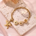 Goldenes Seestern- und Muschel-Armband mit weißer Perle auf beigem Travertinstein - Seestern Muschel Armband / Gold Armband