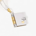 Macro view of book-shaped pendant featuring gold and silver tones and heart cutout - Gold & Silver