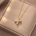 Elegante goldene Kette mit X-Buchstaben-Anhänger und Zirkonia auf Champagner-Seidenhintergrund - Buchstabe X