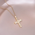 Detailed close-up of golden cross necklace with white crystals on pink satin backdrop - Multiple White Stone Prong Style (X4480)