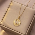 Goldene Edelstahlkette mit Buchstaben-W-Anhänger und Kristallbesatz auf Champagner-Satin - Gold - Buchstabe W