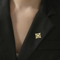 Broche de nudo de bruja dorado con diseño geométrico calado sobre una solapa negra - Nudo de Bruja Dorado