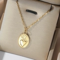 Nahaufnahme eines goldenen Herz-Reliefanhängers an einer geschichteten Edelstahlkette - Vintage Ovales Heiliges Herz Stil (T0496)