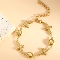Detail shot of golden cross and teardrop charms on a polished stainless steel bracelet - Cross Interval (SL-020) / Gold