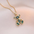 Detail of 18K gold teddy bear pendant set with olive green crystals on pink silk fabric - Emerald Green (X1363)