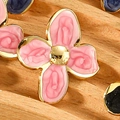 Macro view of pink enamel flower earring with gold edges on a wooden texture background - Pink