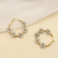 Détail de créoles dorées avec fleurs en perles de cristal gris sur fond beige clair - Transparent